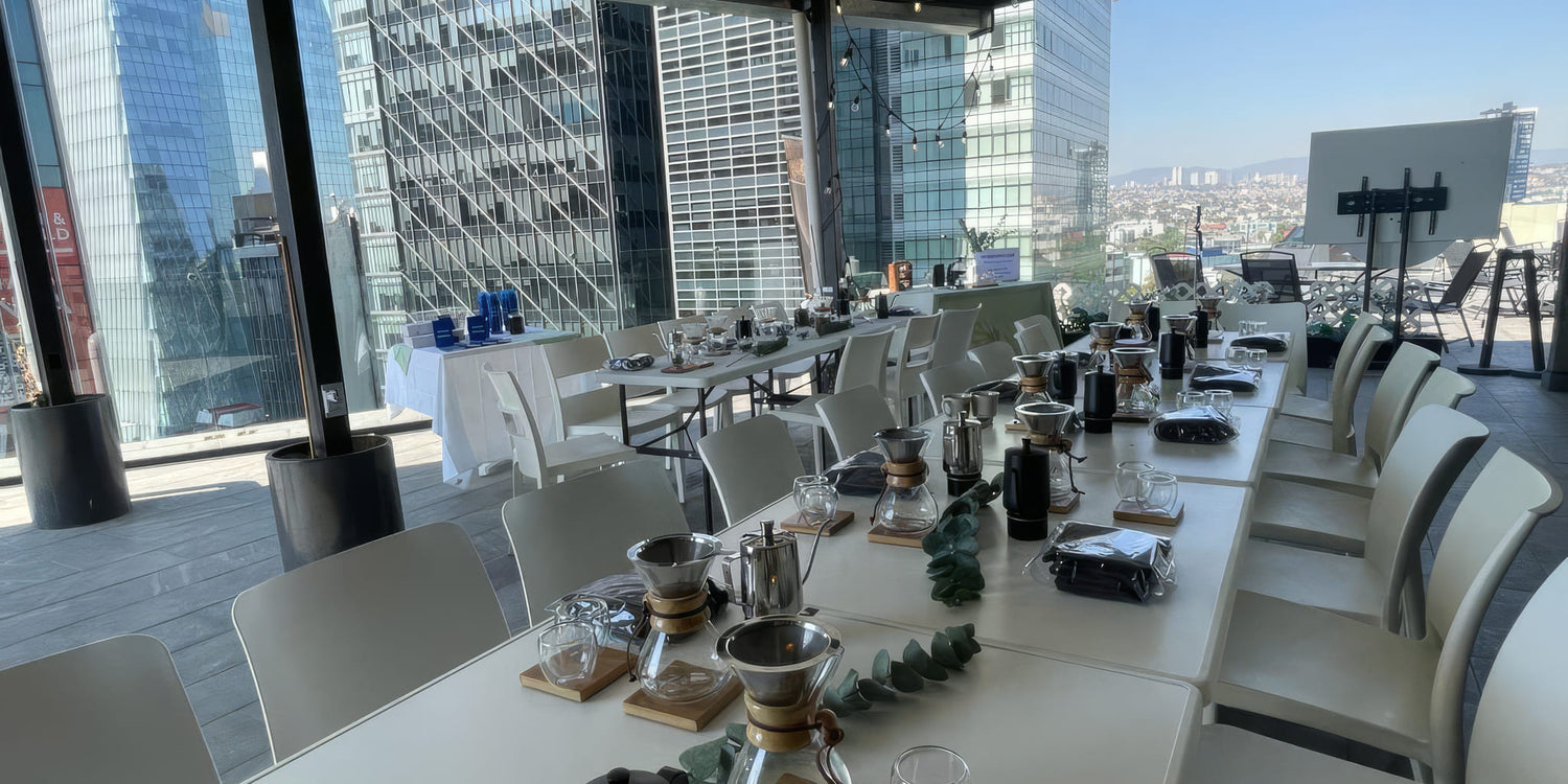 Mesas montadas para una cata en una terraza de Ciudad de México, con estaciones de Chemex y el skyline al fondo